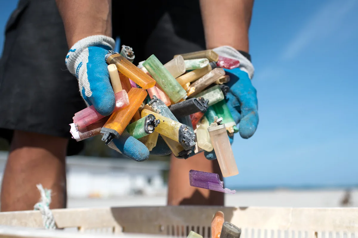 Gloved hands holding discarded cigarette lighters in different colours during a marine-debris sorting exercise.